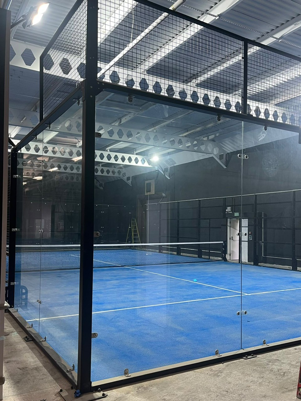 The first padel court installed, with blue surface, glass walls and net up